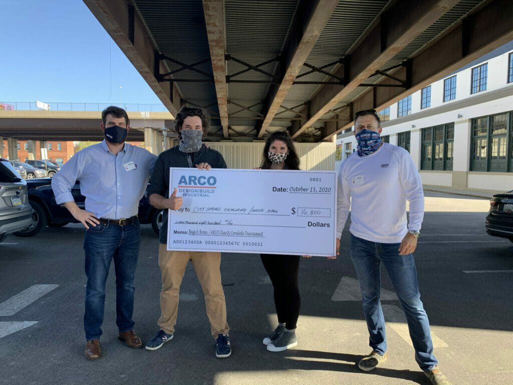 Four people holding a large check for $16,800 donated by ARCO Design/Build for City Spaces Elementary's charity event.