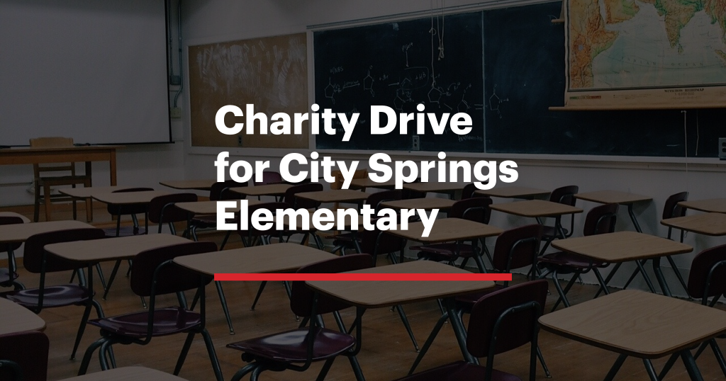 Empty classroom promoting a charity drive for City Springs Elementary with chairs, desks, and a chalkboard in the background.
