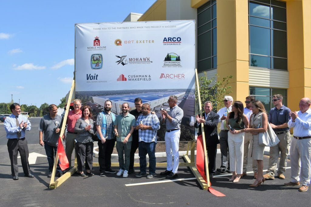 Ribbon cutting in front of sign at new warehouse for Noble House Home Furnishings