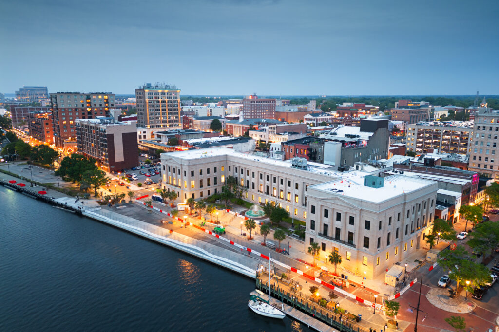 Aerial view of Wilmington at dusk with historic buildings, illuminated streets, and riverfront.