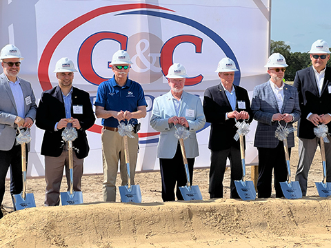 Seven men with hard hats and shovels at construction site groundbreaking in front of C&C banner.